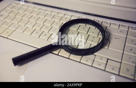 Close up of a magnifying glass on an old laptop keyboard. Computer search engine. Browsing network for answer to every question. Finding useful inform Stock Photo