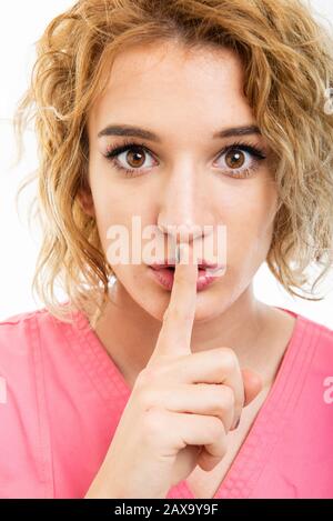 Close-up of nurse wearing pink scrub making silence gesture isolated on white background Stock Photo