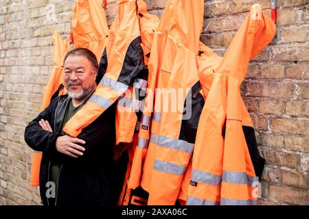 Berlin, Germany. 11th Feb, 2020. Ai Weiwei, Chinese artist, is standing in front of the work in the 'version wall' during the presentation of his artwork 'Safety Jackets Zipped the Other Way' in his studio. The various constructions of safety jackets, hooks and iron bars can be purchased as individual parts from the sponsor Hornbach and assembled by interested parties themselves. Credit: Christoph Soeder/dpa/Alamy Live News
