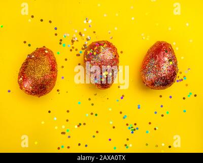 Premium gold Set of 3 golden red easter eggs painted with innovative acrylic on yellow background Ester concept. Top view Stock Photo
