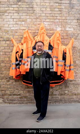 Berlin, Germany. 11th Feb, 2020. Ai Weiwei, Chinese artist, is standing in the studio in front of his artwork 'Safety Jackets Zipped the Other Way' in the 'version wall'. The various constructions of safety jackets, hooks and iron bars can be purchased as individual parts from the sponsor Hornbach and assembled by interested parties themselves. Credit: Christoph Soeder/dpa/Alamy Live News Stock Photo