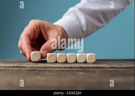 Male hand placing 6 blank wooden dices in a row on rustic wooden desk. With copy space. Stock Photo