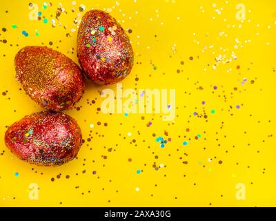 Premium gold Set of 3 golden red easter eggs painted with innovative acrylic on yellow background Ester concept. Top view Stock Photo