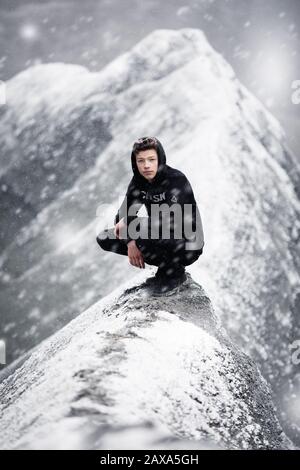 Teenager on a mountain ridge small and narrow path. Winter setting in the alps during a snow storm Stock Photo