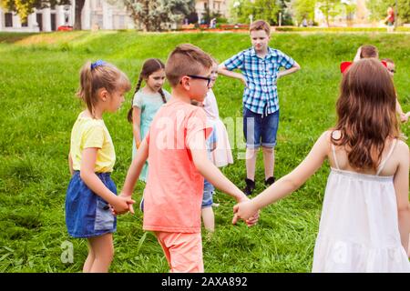 Group of children holding hands and dancing in circle on green lawn Stock Photo