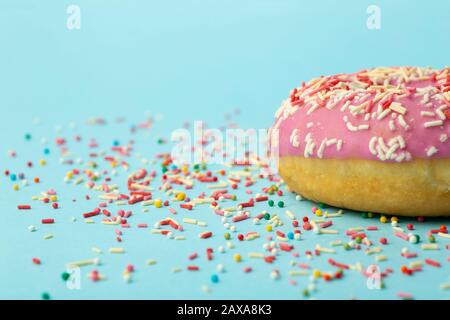 Donut (doughnut) of different colors on a blue background with multi-colored festive sugar sprinkles. Holiday and sweets, baking for children, sugar c Stock Photo