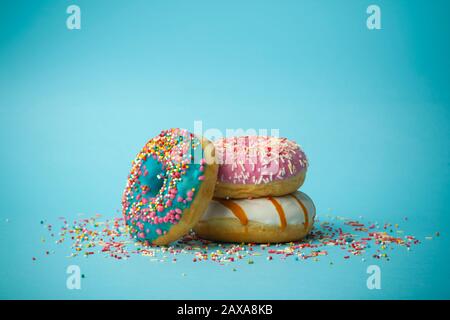Donuts (doughnuts) of different colors on a blue background with multi-colored festive sugar sprinkles. Holiday and sweets, baking for children, sugar Stock Photo