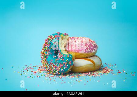 Donuts (doughnuts) of different colors on a blue background with multi-colored festive sugar sprinkles. Holiday and sweets, baking for children, sugar Stock Photo