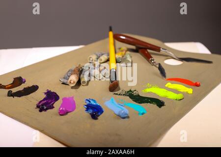 Oil painting. Palette with paints and brushes. The main tools of artist brush and palette knife. Squeeze out oil paints on a palette Stock Photo