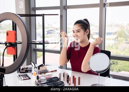 Happy beautiful Asian internet influencer online streaming her cosmetic review content. Stock Photo