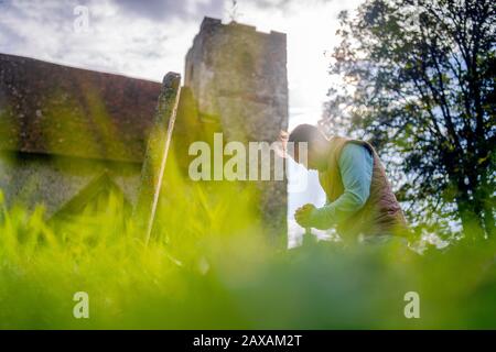 A young man grieving in the front of gravestone on the old cemetery Stock Photo