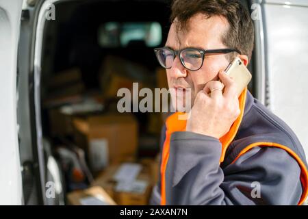 Delivery man talking on the phone in front of his car full of boxes Stock Photo