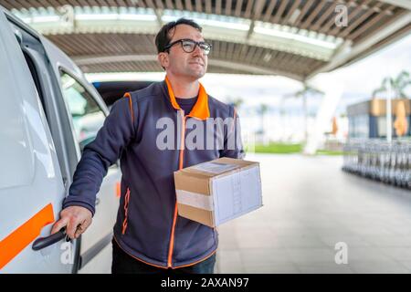 Delivery man leaving his car with a parcel in business area Stock Photo