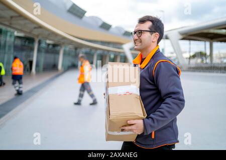 Happy courier with a parcel  delivering to a business area Stock Photo