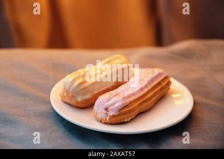 Fresh sweet eclairs with icing on a white ceramic plate on a gray background. Junk food Stock Photo