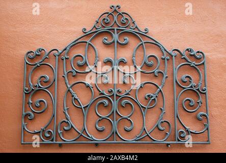 A Decorative Piece of Wrought Iron Mounted to a Bright Colored Stucco Wall Stock Photo