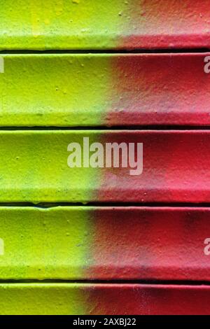 Grunge rusty metal shutter gate with red and yellow paint. Texture, background. Close up. Vertical. Stock Photo