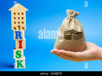Wooden blocks with the word Risk and a miniature house with money bag. Real estate investment risks. Risky investments. Loss of property for non-payme Stock Photo