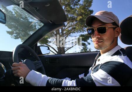 Man with wooden sunglasses and a cap driving a cabriolet Stock Photo