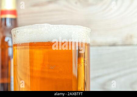 A mug with beer and foam against the background of a bottle and a wooden background. Stock Photo