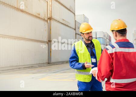 Dock workers talking near cargo containers at sunny shipyard Stock Photo