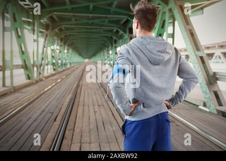 Young male runner standing on train tracks with hands on hips Stock Photo