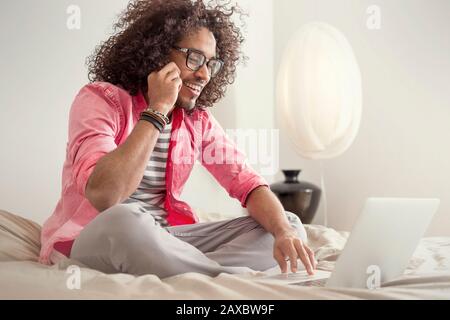 Happy young man using laptop on bed Stock Photo