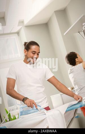 Young man doing laundry, ironing shirt in laundry room Stock Photo