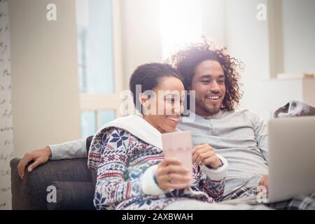 Affectionate couple in pajamas relaxing, using laptop on sofa Stock Photo