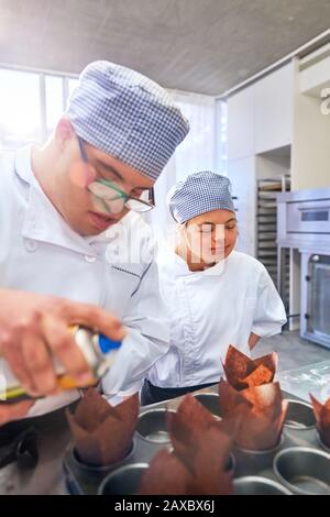 Students with Down Syndrome baking muffins in kitchen Stock Photo