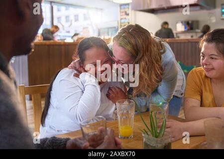 Happy mentor and young women with Down Syndrome laughing in cafe Stock Photo