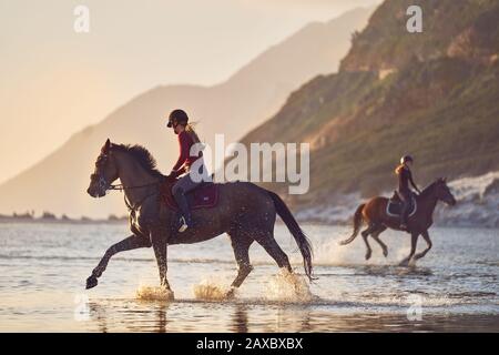 Young women horseback riding in ocean surf Stock Photo