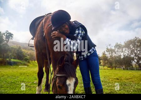 Happy girl hugging horse in rural grass paddock Stock Photo