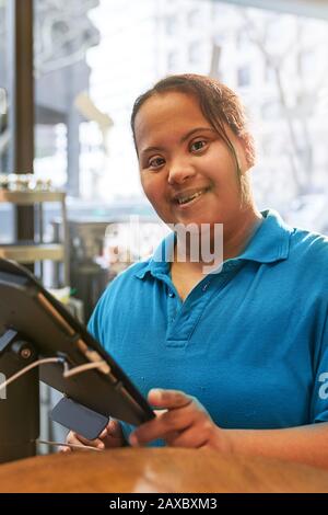 Portrait confident young woman with Down Syndrome working in cafe Stock Photo