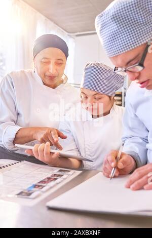Chef and students with Down Syndrome using digital tablet in kitchen Stock Photo