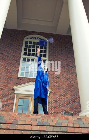 Vertical shot of a male in a blue mantle throwing his graduation cap up in the air Stock Photo
