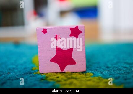 Pink square toy with stars on its surface put on a multicolored surface Stock Photo