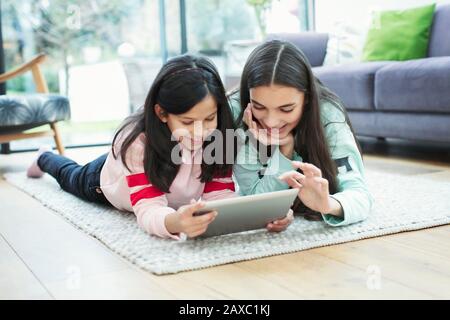 Smiling sisters using digital tablet on living room floor Stock Photo