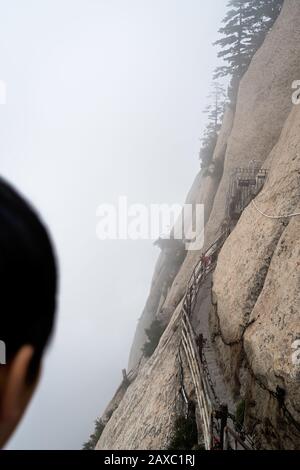 Huashan, China -  August 2019 : Unidentified chinese person looking at the stone steps cut on a side of a mountain rock leading to the dangerous and p Stock Photo