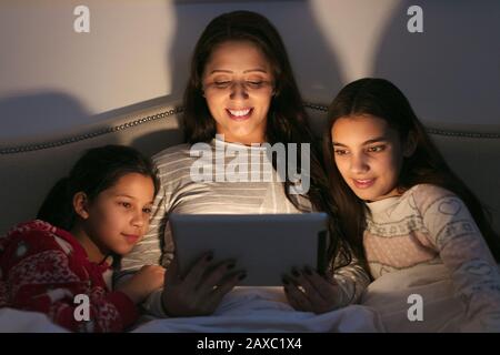 Mother and daughters using digital tablet in dark bedroom Stock Photo