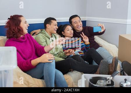 Happy friends taking a break from moving, taking selfie on sofa Stock Photo