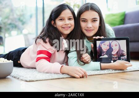 Portrait smiling sisters using digital tablet camera on living room floor Stock Photo