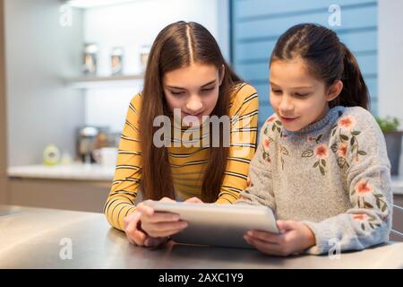 Sisters using digital tablet in kitchen Stock Photo