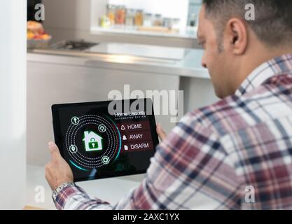 Man setting smart home security alarm from digital tablet in kitchen Stock Photo
