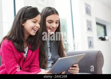 Happy sisters using digital tablet on living room sofa Stock Photo