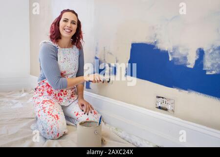 Portrait happy woman in overalls painting wall Stock Photo
