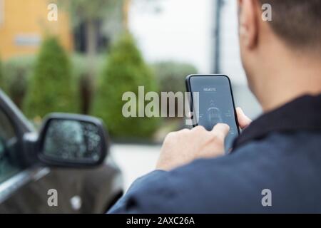 Man setting car alarm from smart phone in driveway Stock Photo