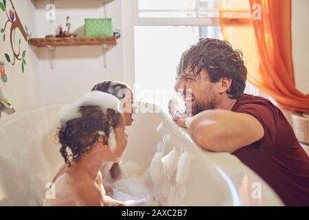 Playful father giving toddler daughters bubble bath