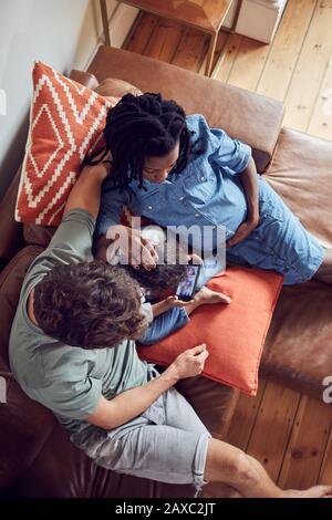 Pregnant young family using smart phone on living room sofa Stock Photo