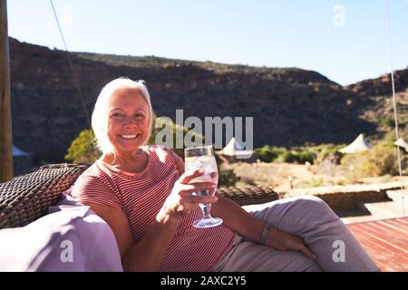 Portrait happy senior woman drinking water on sunny safari hotel patio Stock Photo